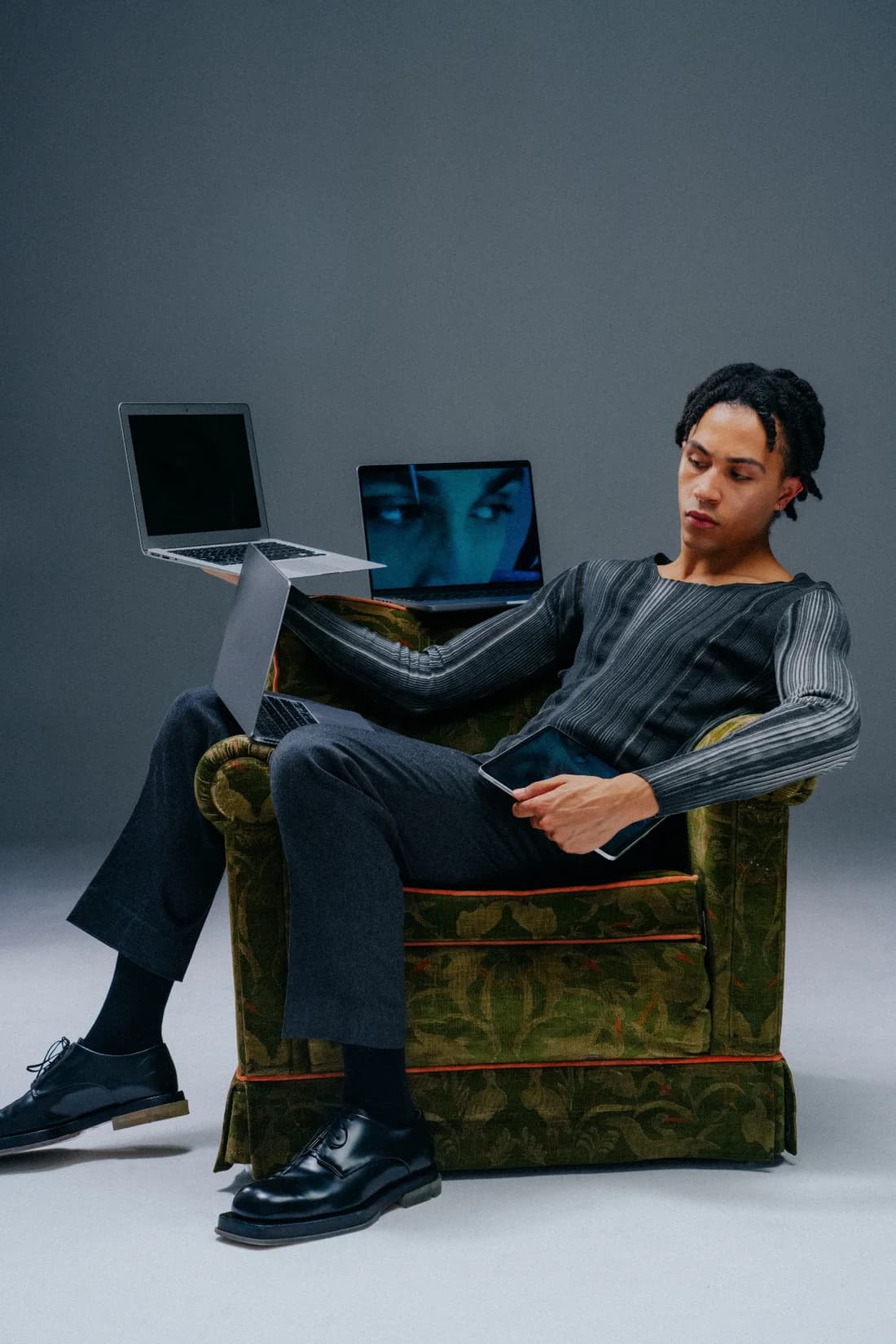 A person sitting in a green armchair with a laptop and a tablet.